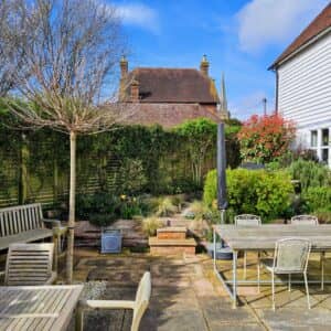 An entertaining space in Frittenden with plenty of seating surrounded by grasses, herbaceous planting and climbers with a feature tree to provide shade